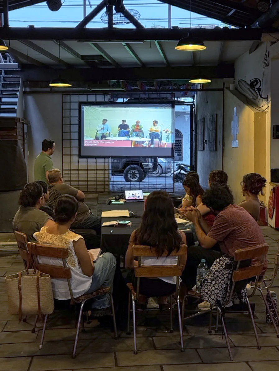 Participantes del taller sentados de espaldas frente a una pantalla en Espacio Cultural 399, viendo una conversación con el fotógrafo Pablo Ortiz Monasterio.