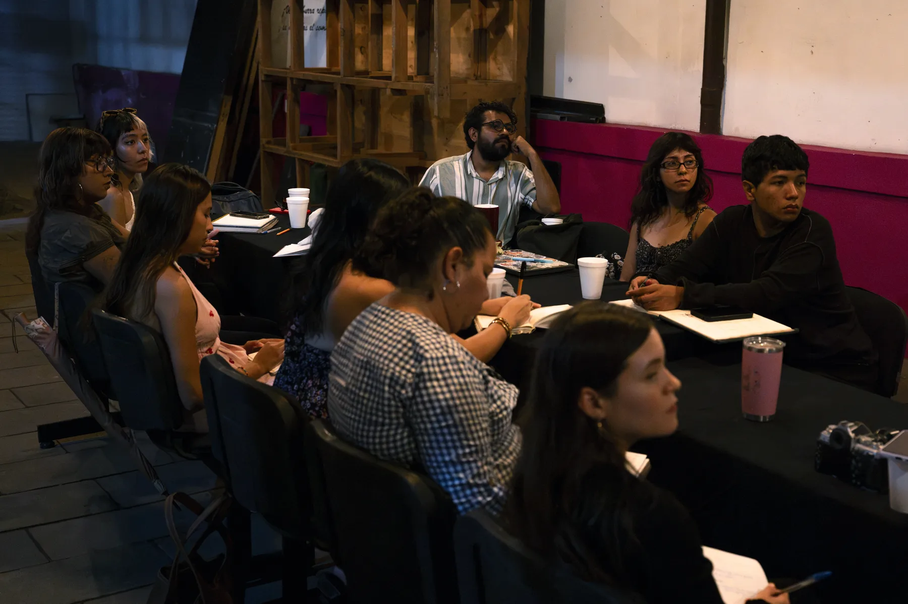Participantes alrededor de una mesa con libretas y vasos de café, escuchando con atención; algunas personas toman notas.